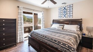 Une chambre à coucher comprenant un lit, une commode, un ventilateur de plafond, une table de chevet et une vue sur l’extérieur.
