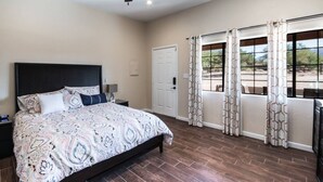 Une chambre  à coucher comprenant un lit, une table de chevet, un ventilateur de plafond, une porte et une fenêtre avec des rideaux.