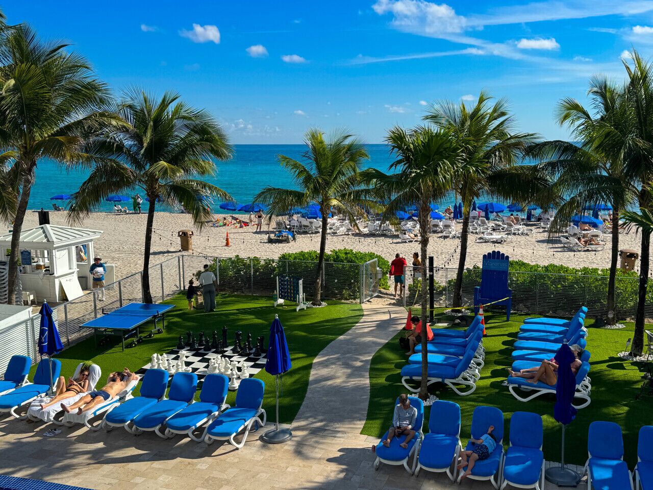 A beachside resort with sun loungers, palm trees, and a view of the ocean.