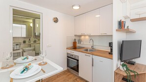 A compact kitchen with a dining area, a built-in oven, a sink, and a television on a wooden stand. - 3 bedroom beautiful home in Rogoznica (Rogoznica)