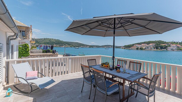 A balcony with a table and chairs, an umbrella, and a view of the sea and hills. - 3 bedroom beautiful home in Rogoznica (Rogoznica)