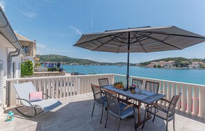 A balcony with a table and chairs, an umbrella, and a view of the sea and hills. - 3 bedroom beautiful home in Rogoznica (Rogoznica)