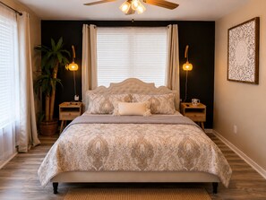 Une chambre à coucher avec un grand lit, deux lampes de chevet, un ventilateur de plafond et une grande fenêtre avec des stores.