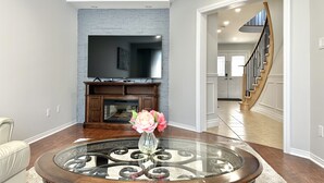 A living room with a fireplace, a television mounted above it, and a round coffee table with a vase of flowers. - Soléra — A Light-Filled Minimalist Escape Near Beaches & Golf (Innisfil)