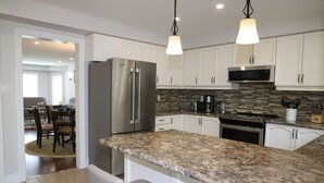 A modern kitchen with white cabinets, a granite countertop, stainless steel appliances, and pendant lighting. - Soléra — A Light-Filled Minimalist Escape Near Beaches & Golf (Innisfil)