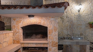 Cocina exterior de piedra con horno de pizza integrado, un lavadero y una pequeña encimera.