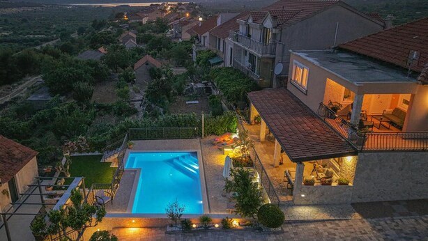 Zona residencial con piscina, jardín bien cuidado y casas con techos de tejas rojas.