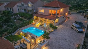 Una casa de dos pisos con piscina, mobiliario de exterior y un coche aparcado cerca.