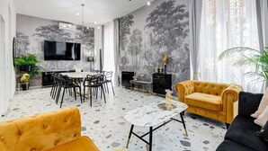 Ett modernt vardagsrum med en matplats, en tv som är monterad på väggen och ett stort fönster med gardiner.
