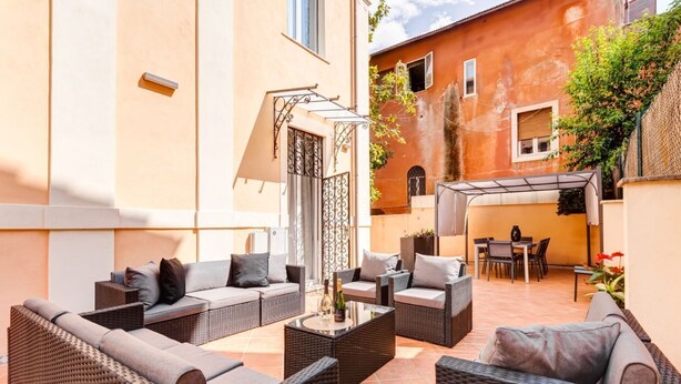 En uteplats med möbler i rotting, ett soffbord i glas och en pergola.