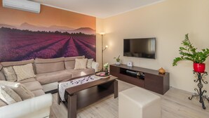 Una sala de estar con sofá, mesa de centro, televisor y un mural de un campo.