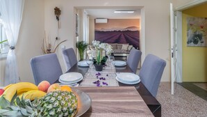 Comedor con mesa lista para cuatro personas, un sofá al fondo y vistas de un viñedo a través de una ventana.