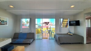 A hotel room with a sofa, a bed, a TV, and a balcony with a view of buildings and palm trees. - Porto de Galinhas Maracaipe, close to the sea. (Ipojuca)