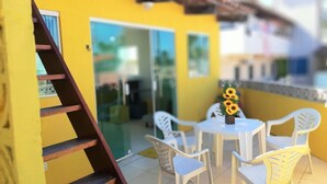 A yellow building with a glass door entrance, white plastic chairs, and a table with a vase of sunflowers. - Porto de Galinhas Maracaipe, close to the sea. (Ipojuca)