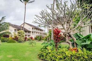 A hotel with multiple-story buildings, a well-maintained garden with various plants and a palm tree, and a clear sky.