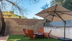 Une terrasse extérieure avec un mur en briques, une table avec des chaises et un grand parasol.