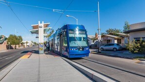 Un tramway dans une station, avec un ciel dégagé, un passage piéton et un bâtiment sur lequel on peut lire l’inscription « CUISINE ».