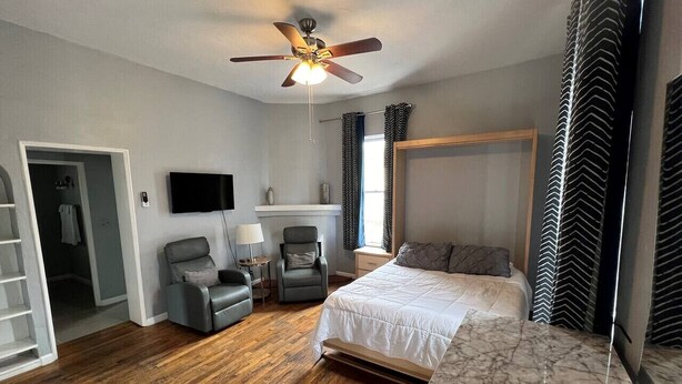 Une chambre à coucher comprenant un lit, deux chaises, un ventilateur de plafond, un téléviseur et une armoire.