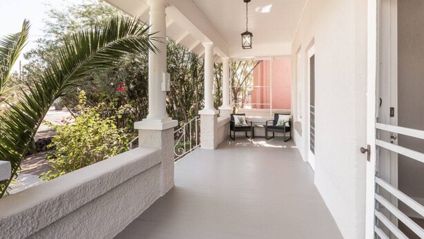 A covered outdoor area with a table and chairs, white columns, and a view of greenery. - Historic Jostaad Home! (Tucson)