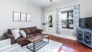 A living room with a brown leather sofa, a wooden coffee table, a TV on a blue cabinet, and a ceiling fan. - Historic Jostaad Home! (Tucson)