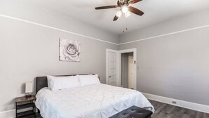 A bedroom with a bed, a nightstand, a bench, a ceiling fan, and a door. - Historic Jostaad Home! (Tucson)