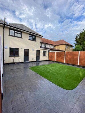 A residential property with a paved patio, a green artificial lawn, and a wooden fence.