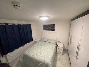 A bedroom with a bed, a nightstand, a wardrobe, a radiator, and a picture of a bridge.