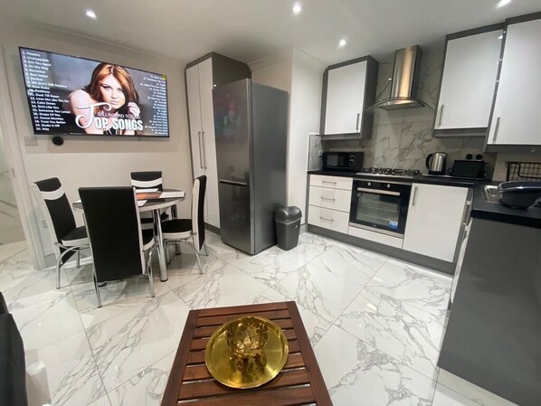 A modern kitchen with a TV, dining area, and a marble floor.