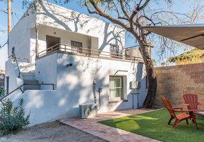 Un bâtiment blanc doté d’un balcon, d’une petite fenêtre et d’un patio aménagé avec des chaises.