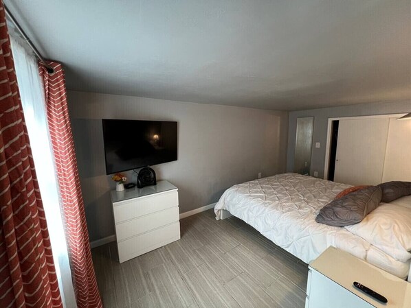 Une chambre à coucher avec un lit, une commode, un téléviseur fixé au mur et une porte.