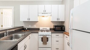 A compact kitchen with white cabinets, a gas stove, a microwave, and a refrigerator.