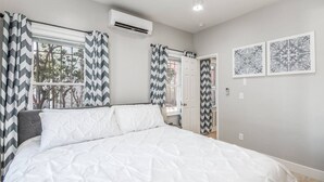 A bedroom with a bed, air conditioning unit, and two doors.