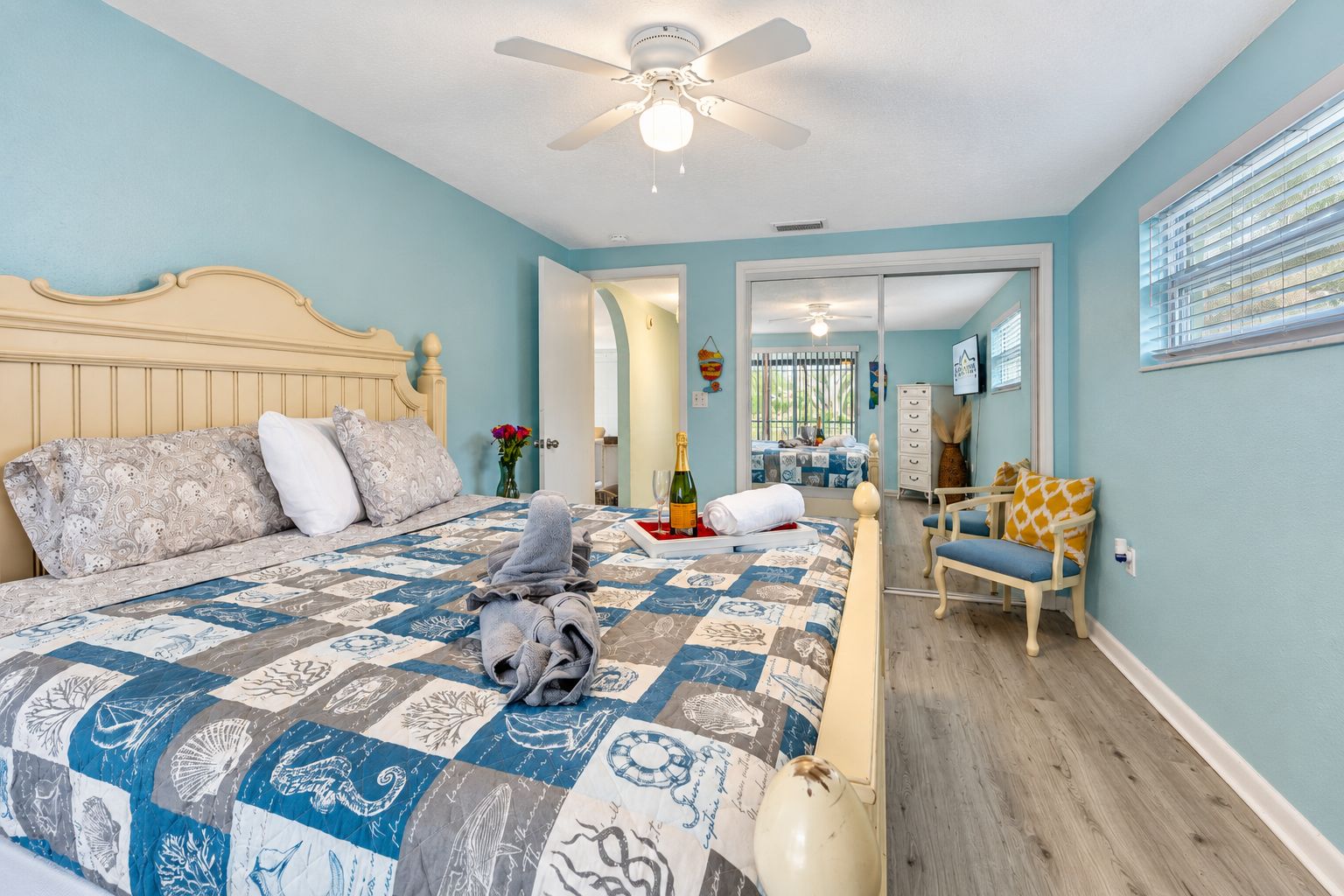 A bedroom with a large bed, a ceiling fan, a chair, and a window with blinds.