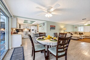 A spacious living area with a dining table set for four, a kitchen with modern appliances, and a ceiling fan. - Cozy Oasis Screened Pool Picturesque Water Canal Views! (Port Richey)