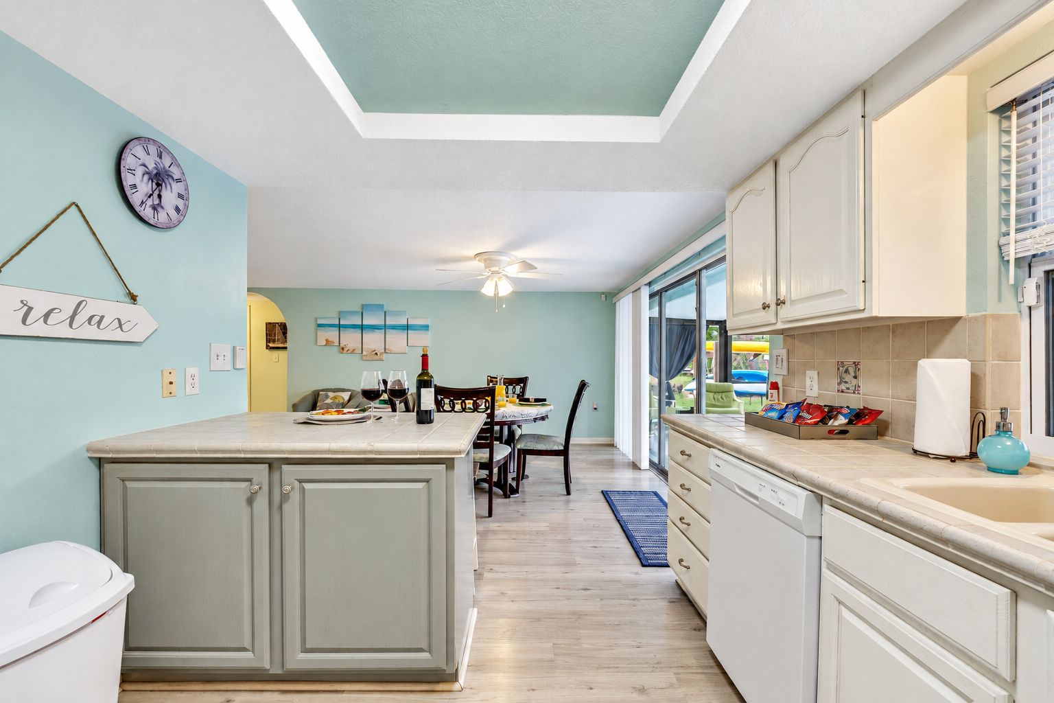A kitchen with a central island, a dining area with a table and chairs, and a view through the glass door.