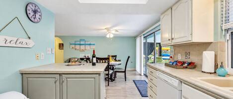 A kitchen with a central island, a dining area with a table and chairs, and a view through the glass door.