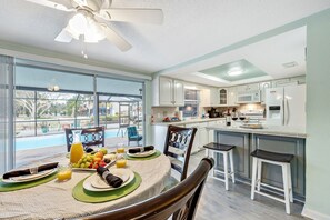 A dining area with a table set for two, a kitchen with modern appliances, and a view of a swimming pool. - Cozy Oasis Screened Pool Picturesque Water Canal Views! (Port Richey)