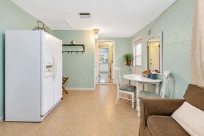 A compact kitchen with a refrigerator, a dining table with chairs, and a small island with a plant. - Cozy Oasis Screened Pool Picturesque Water Canal Views! (Port Richey)