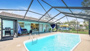 Una piscina con un porche cubierto, mobiliario exterior y una parrilla.