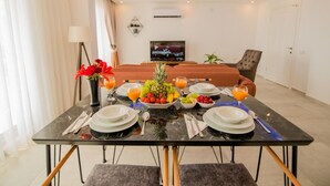 Hotellihuone, jossa on ruokailutila. Tilaan on katettu aamiaispöytä, jossa on hedelmiä, mehua ja lautasia.