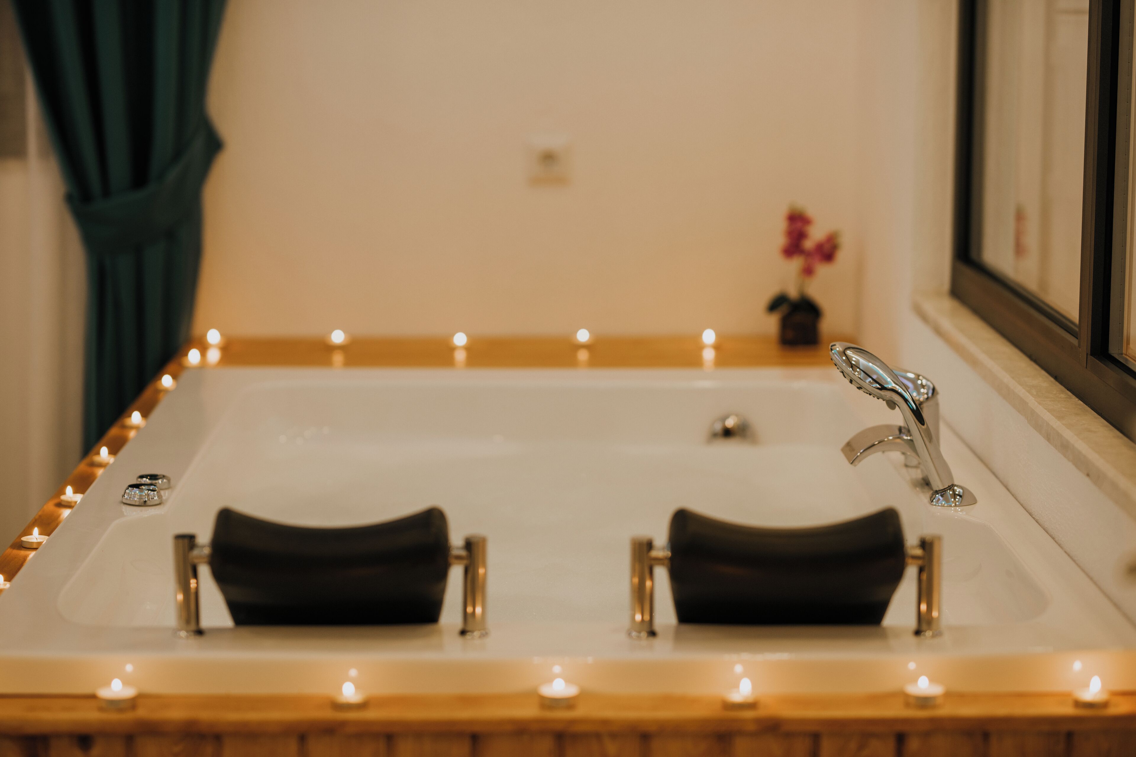 A bathtub with candles, a mirror, and a small vase with flowers.