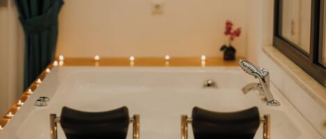 A bathtub with candles, a mirror, and a small vase with flowers.