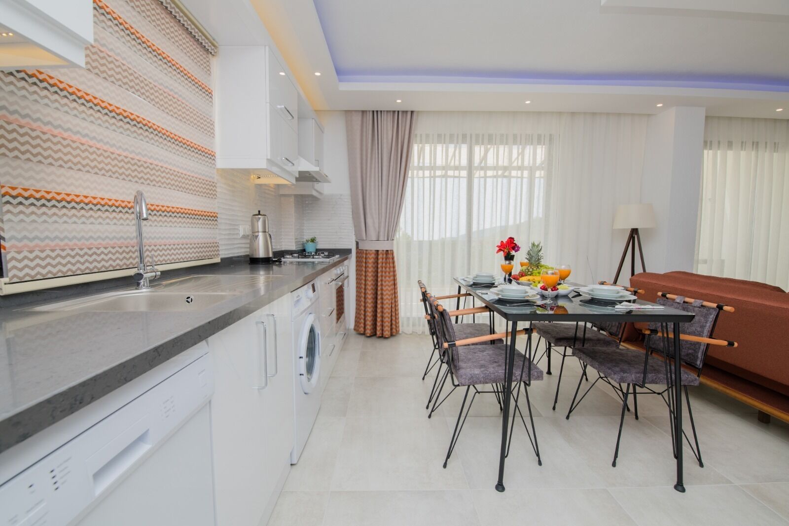 Une cuisine moderne avec un coin repas, comprenant un îlot de cuisine, des appareils électroménagers intégrés et une table à manger avec des chaises.