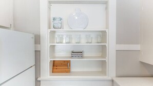 Cocina blanca con unidad de almacenamiento empotrada que contiene un tarro, un plato y varios vasos.