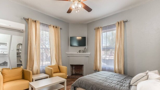 Een slaapkamer met een bed, twee fauteuils, een tafeltje, een open haard en een plafondventilator.