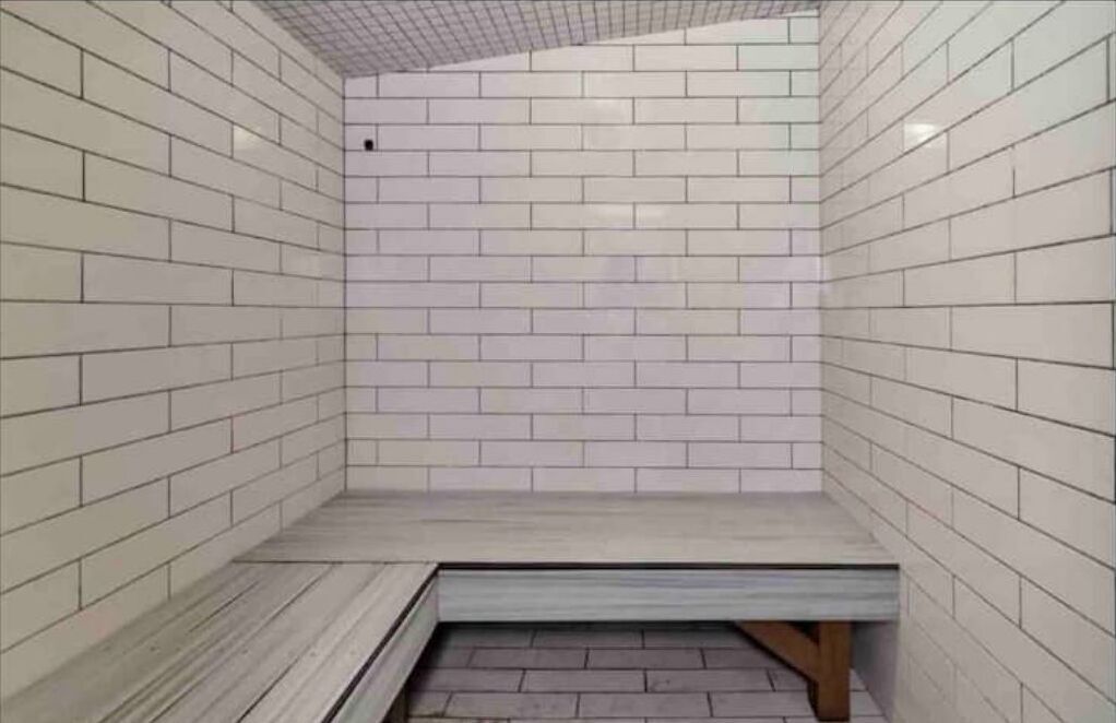 Une salle de bain carrelée avec un banc et une petite fenêtre.