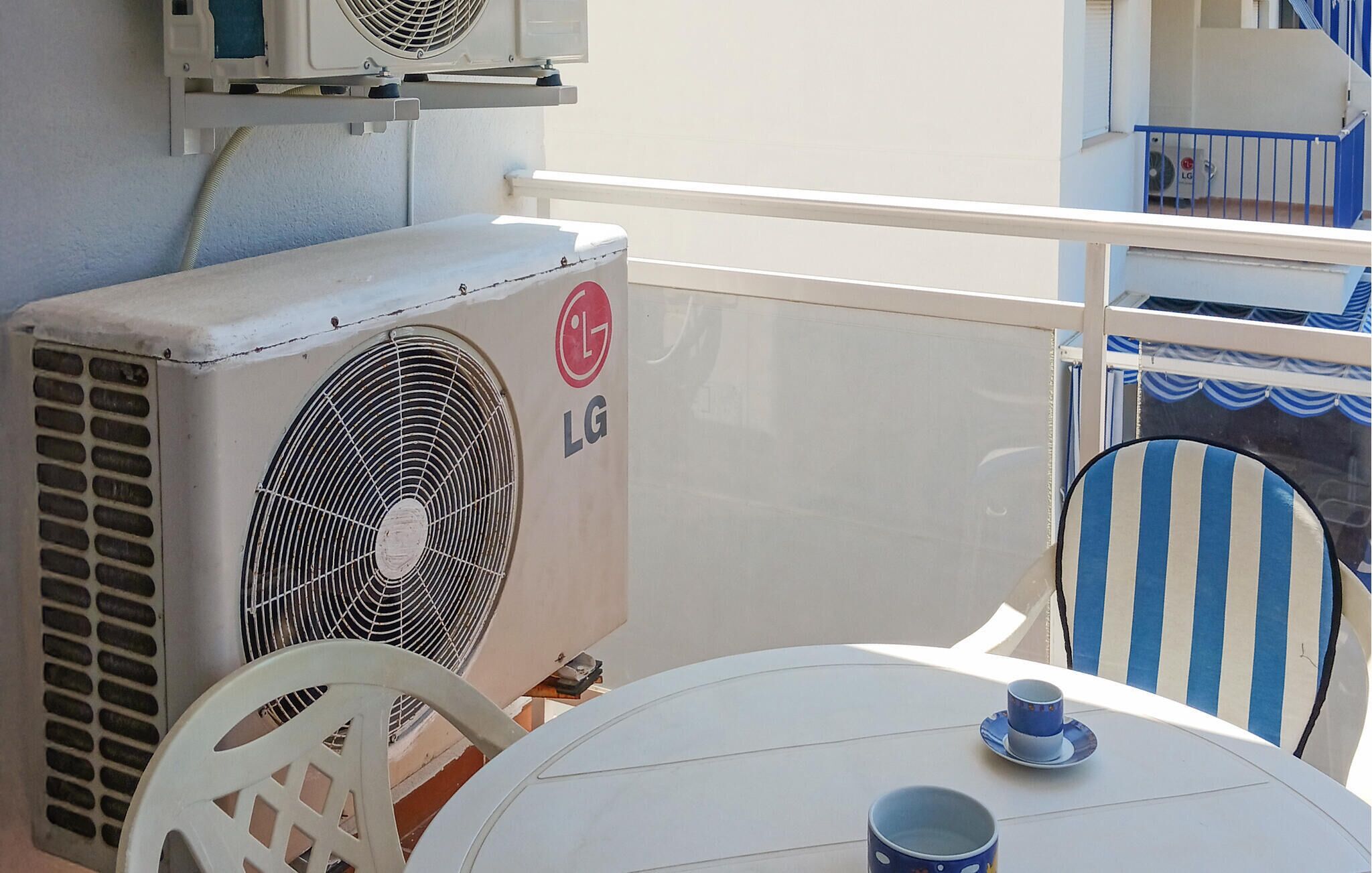 A balcony with two LG air conditioning units, a white table, and a blue-striped chair.