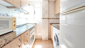 A modern kitchen with granite countertops, a built-in oven, a washing machine, and a microwave. - 2 bedroom beach front apartment in Bellreguard (Bellreguard)