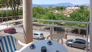 A balcony with a table and chairs, overlooking a street with parked cars and greenery. - 2 bedroom beach front apartment in Bellreguard (Bellreguard)