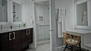 Un baño con tocador de madera oscura, cabina de ducha de vidrio y silla de mimbre.
